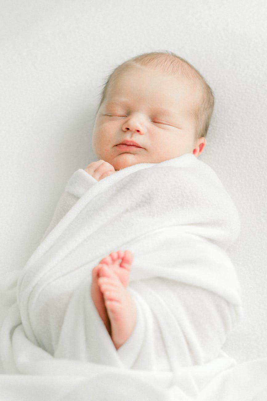 sleeping tiny newborn baby wrapped in a white blanket